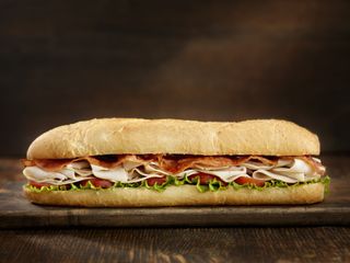 A foot long turkey and bacon sub served on a wooden board.