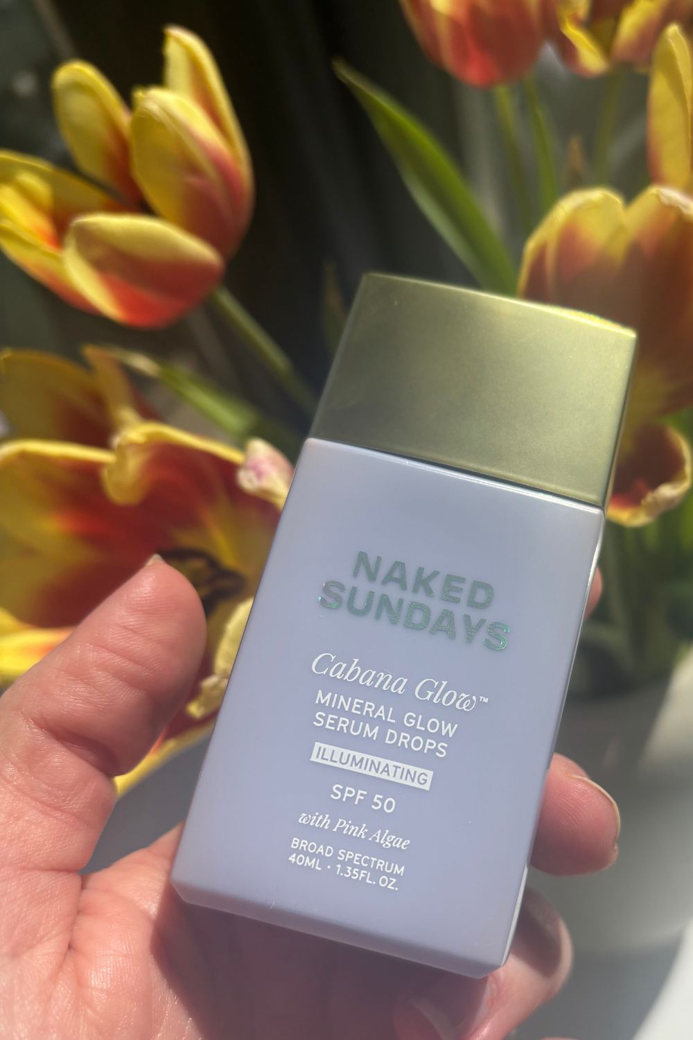 a hand holding a bottle of naked sundays cabanaglow mineral glow serum drops
