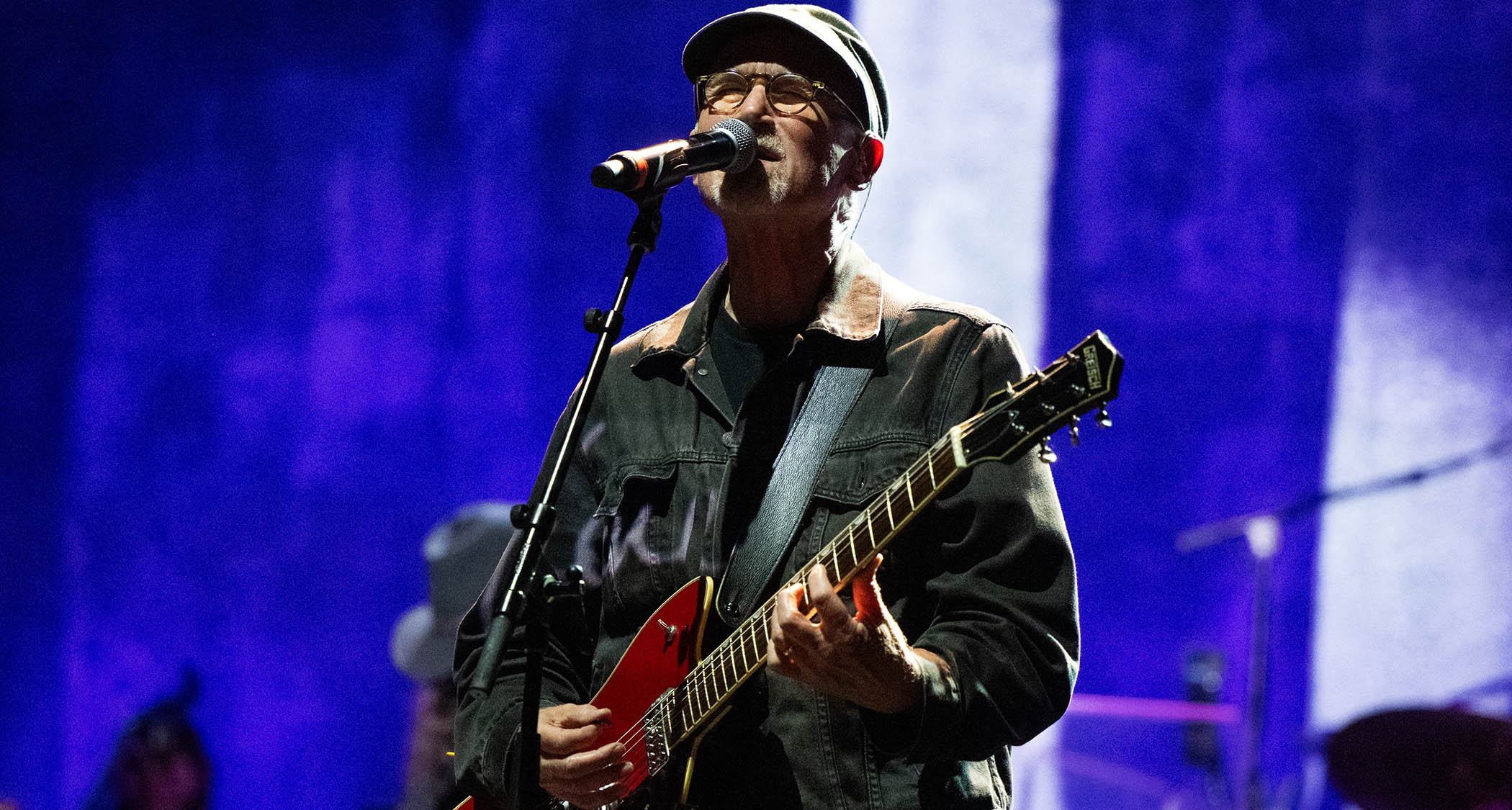 Marshall Crenshaw wears a skip cap and plays a red Gretsch electric guitar
