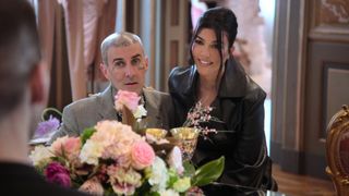 Travis Barker and Kourtney Kardashian sitting happily in behind a bouquet of flowers