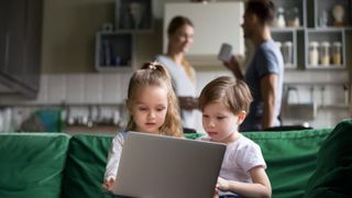 Two children looking at a laptop while their parents talk in the background
