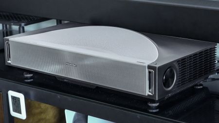 A Hisense PX4 Pro projector on a home media center shelf
