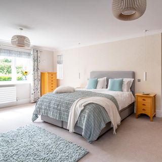 Bedroom with a beautiful garden view containing grey fabric storage bed and pillows with matching loose carpet on the full light brown carpet