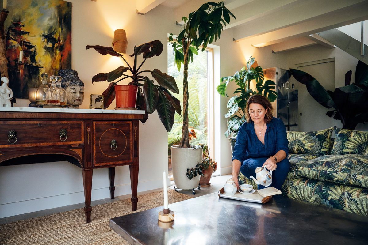 A woman sat on a sofa looking at a book in a lounge filled with reclaimed furniture and houseplants