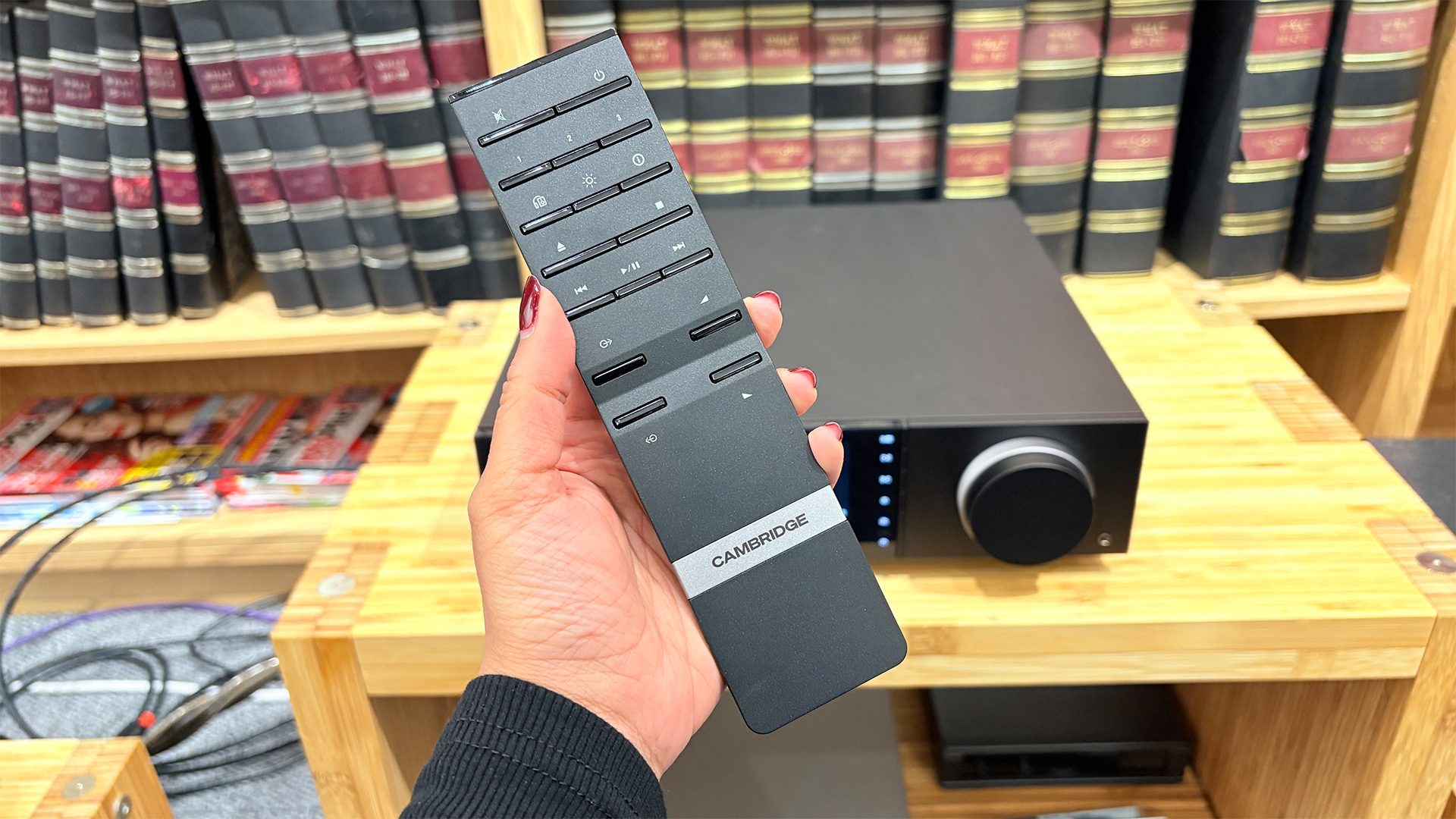 Cambridge Audio Evo 150 SE music streamer in front of bookcase with remote held in hand in foreground