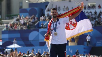 Wrapped in the Serbian flag, Novak Djokovic walks the stage with his medal at Champions Park, on day 10 of the Paris Games