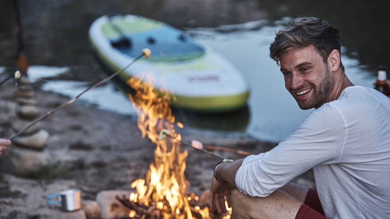 Man toasting marshmallows on a campfire by water