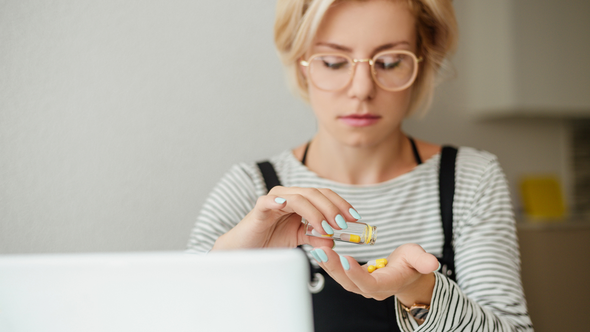 Defocused young woman in eyeglasses pouring out pills from glass bottle on hand.