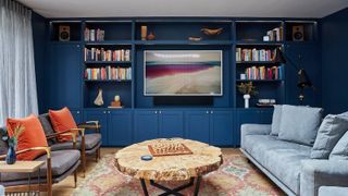 living room with navy built in media wall, blue sofas, and accents of orange throughout the interior design