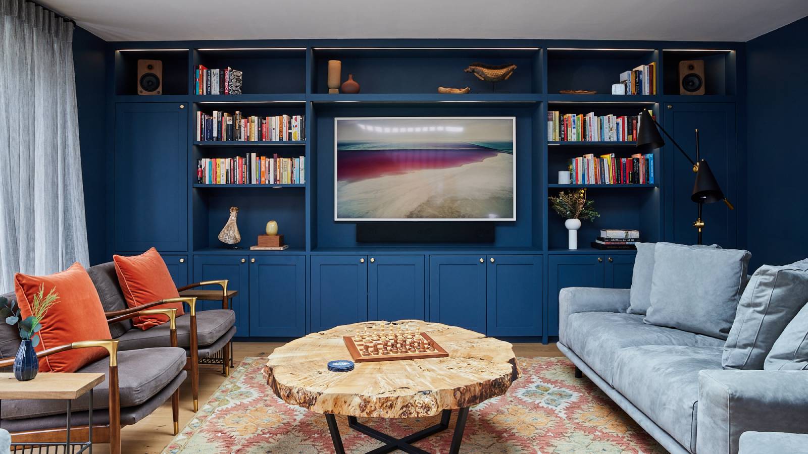 living room with navy built in media wall, blue sofas, and accents of orange throughout the interior design
