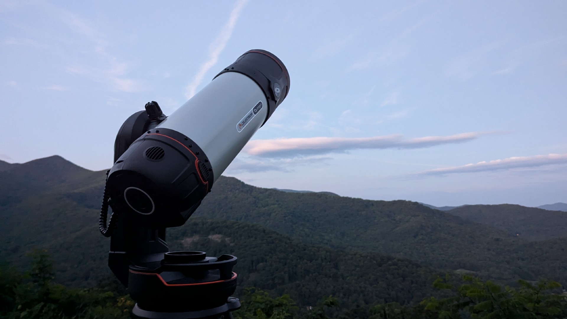 a black and white telescope in a field with trees behind it