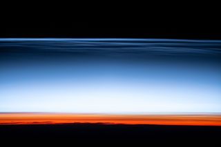 An astronaut at the International Space Station captured this image of noctilucent or "night-shining" clouds in Earth's upper atmosphere. These clouds, which are made of tiny ice crystals, are only visible during astronomical twilight, when the sun just below the horizon, but the clouds are still illuminated by sunlight. Below the blue cloud layer, the lower part of the atmosphere glows with the signature reddish color of sunset.