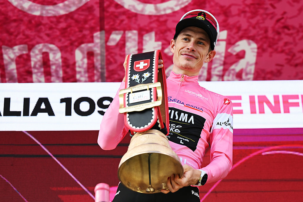 Jonas Vingegaard in the pink jersey on the podium holds a huge bell as prize by the Swiss hosts