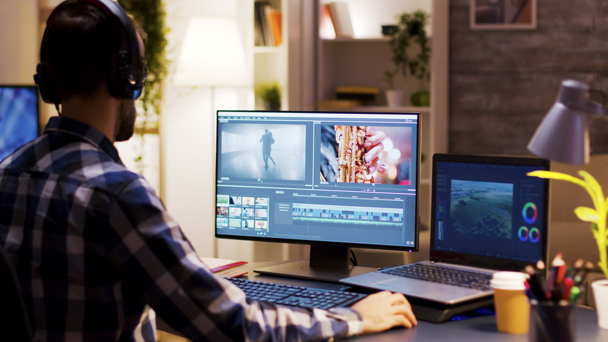 En mann i rutete skjorte sitter foran en MacBook og redigerer en video