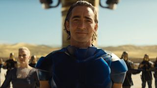 a man in blue armor smiles toward the camera on a desert planet
