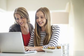 Mother and daughter using laptop together at home, after learning how to talk to children about periods