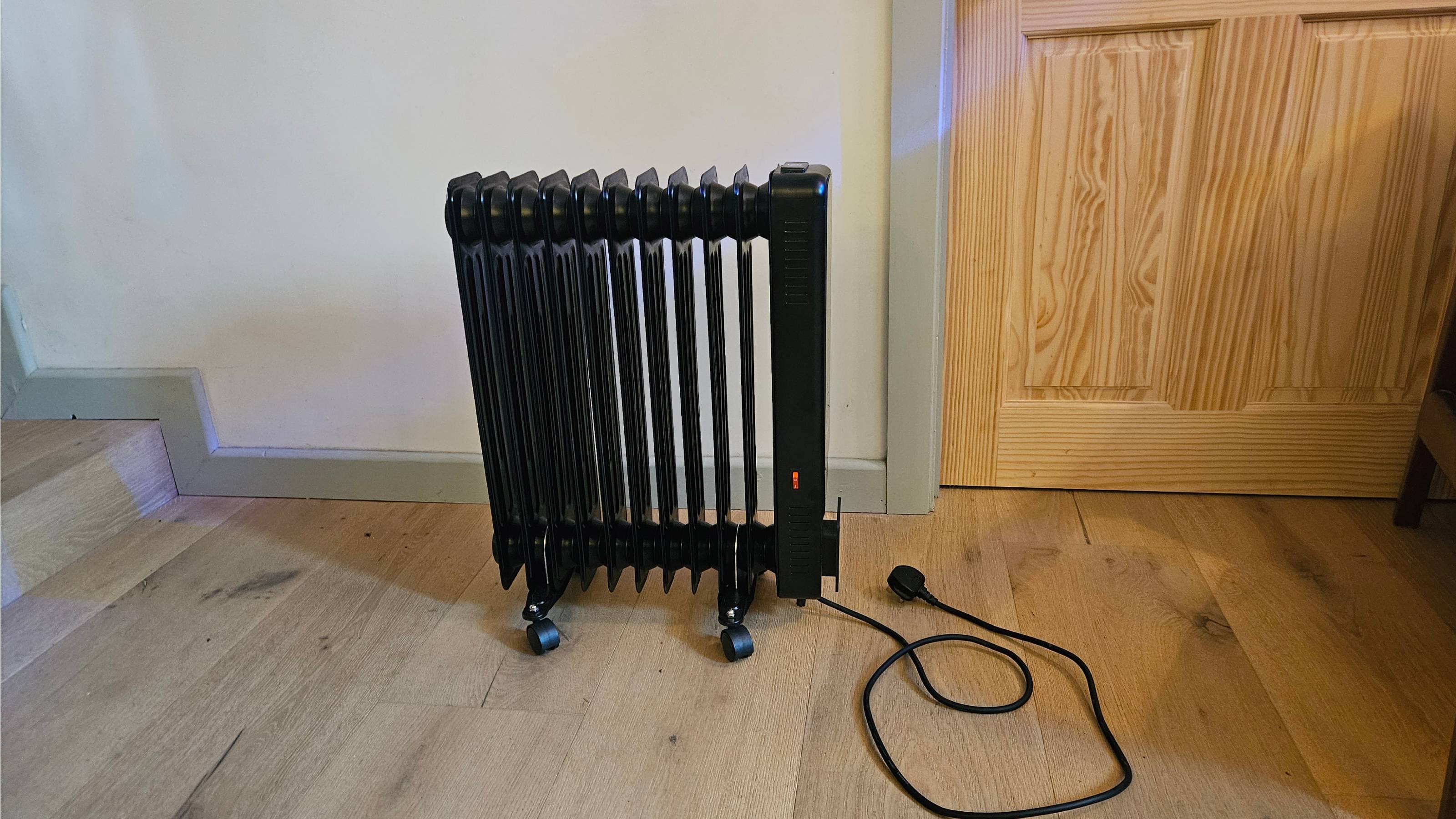 black oil filled radiator in white room with wooden flooring
