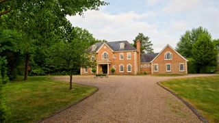 A redbrick detached house with large gravel driveway and lawns either side