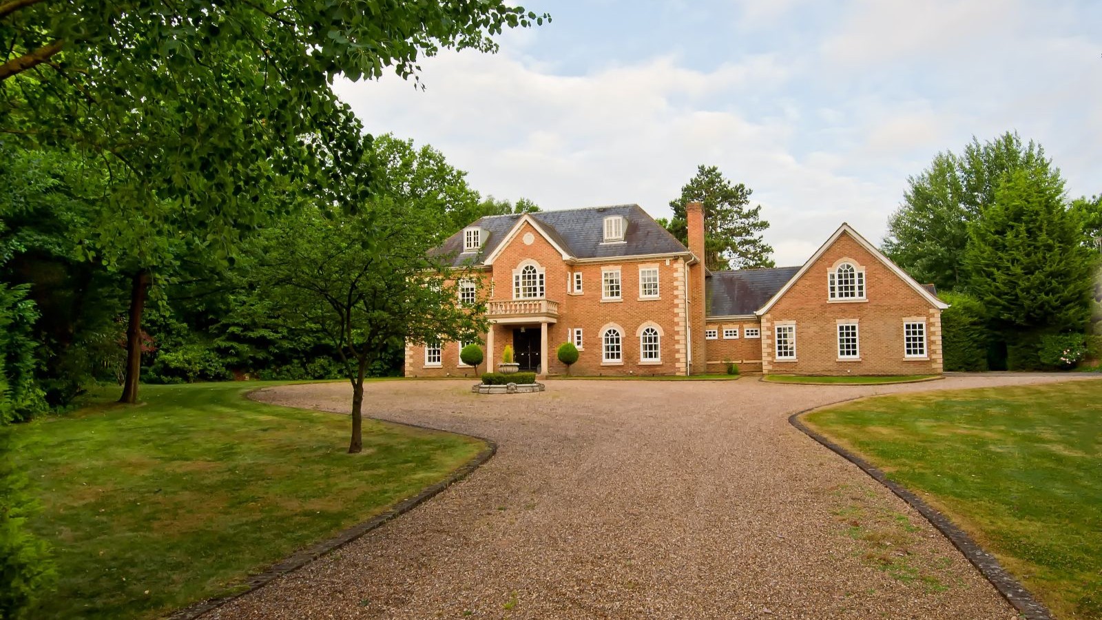 A redbrick detached house with large gravel driveway and lawns either side