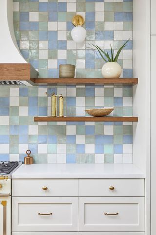 white green and blue tiled kitchen backsplash with open wooden shelves and white cabinets below