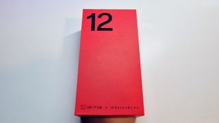 En röd förpackning för OnePlus 12 ligger på ett vitt bord.