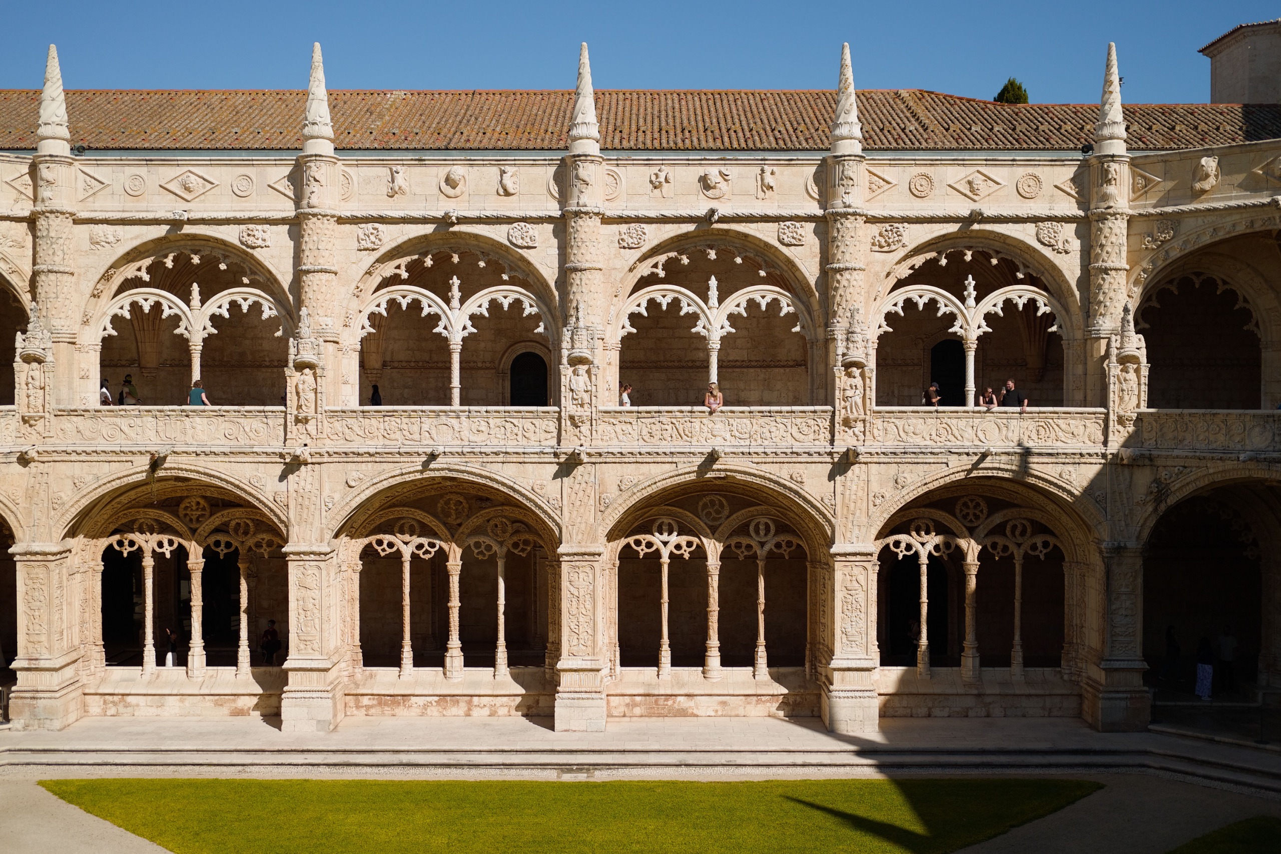 Ornately carved two-story cloister with pointed arches, stone columns and visitors walking along the galleries.