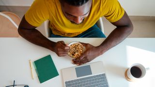 Man sitting in front of a laptop eating cereal