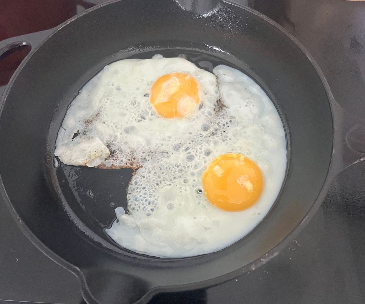 Two large fried eggs with yellow yolks in a black cast iron pan