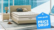 The Saatva Classic mattress pictured in a pool house overlooking a bright blue swimming pool, with a blue price drop sale badge overlaid on the image
