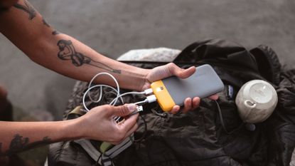 A man plugging his phone into one of the best power banks, the BioLite Charge PD 80