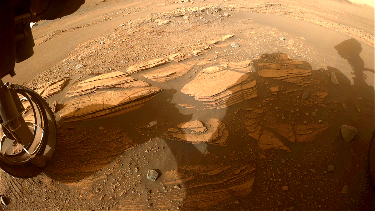 a multi-layered rock on Mars with a rover wheel on the left, all in shadow