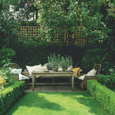 Wooden garden furniture nestled against a green hedge.