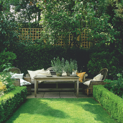 Wooden garden furniture nestled against a green hedge.