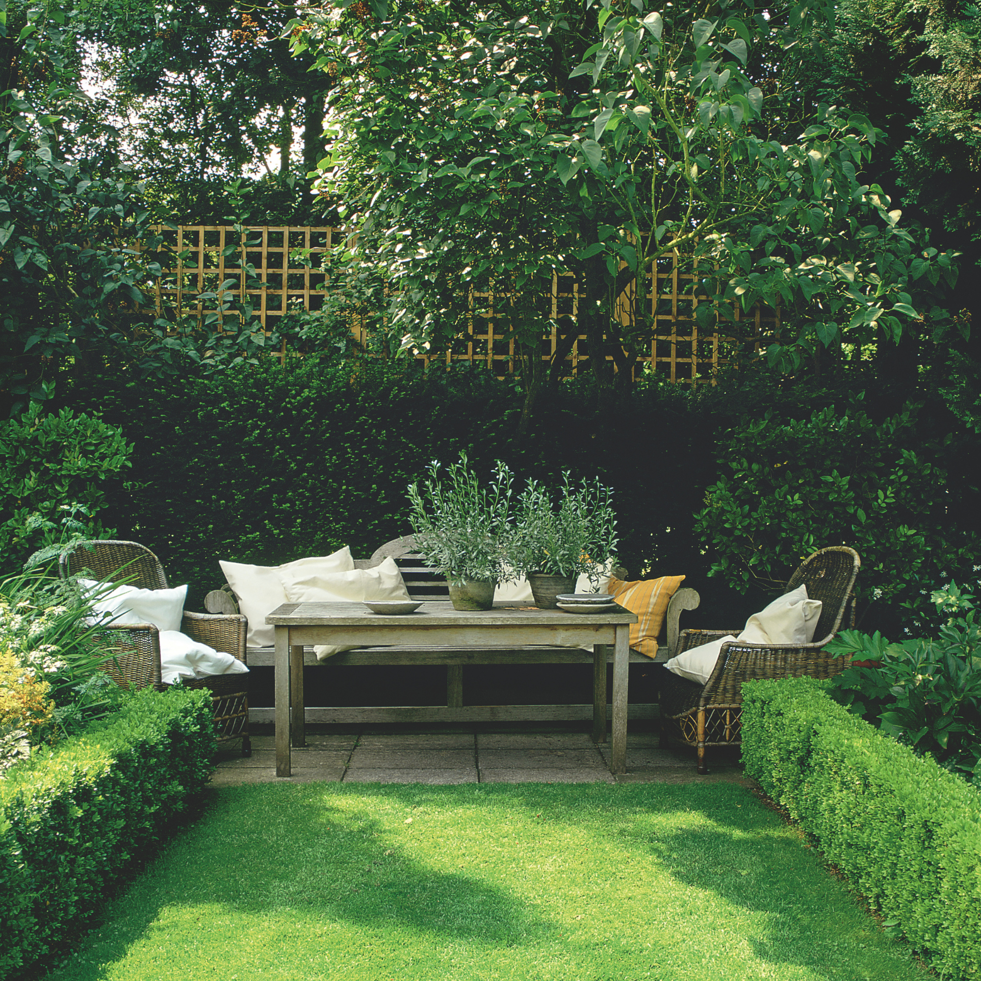 Wooden garden furniture nestled against a green hedge.