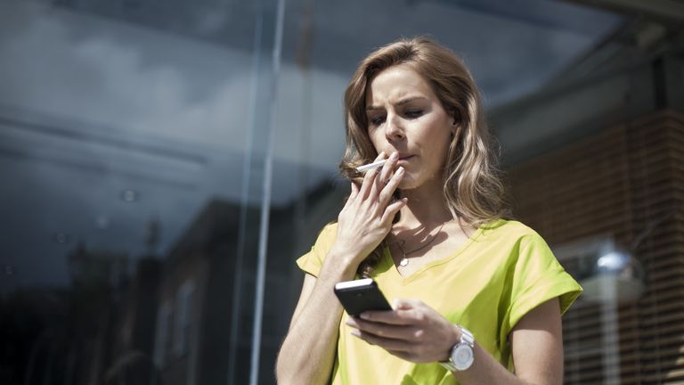 Woman looking at her phone while smoking outside her workplace