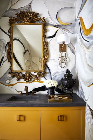 A yellow, black, and white hand-painted bathroom wall with an ornate mirrow