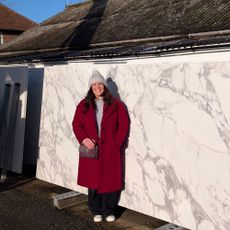 Woman in red coat standing in front of large marble slab
