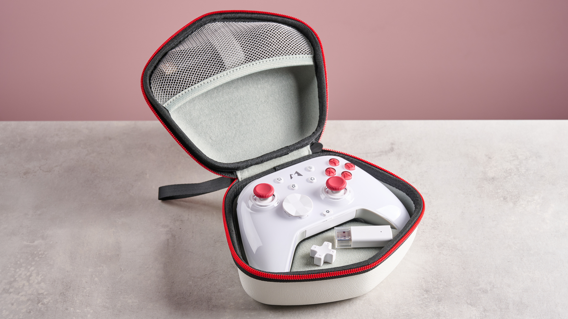 Mobapad Huben 2 in its open case with spare D-pad hat and USB dongle visible, on desk with pink background
