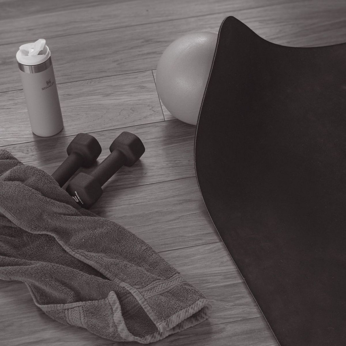 home workout kit on a wooden floor - dumbbells, mat, water bottle, towel, pilates ball