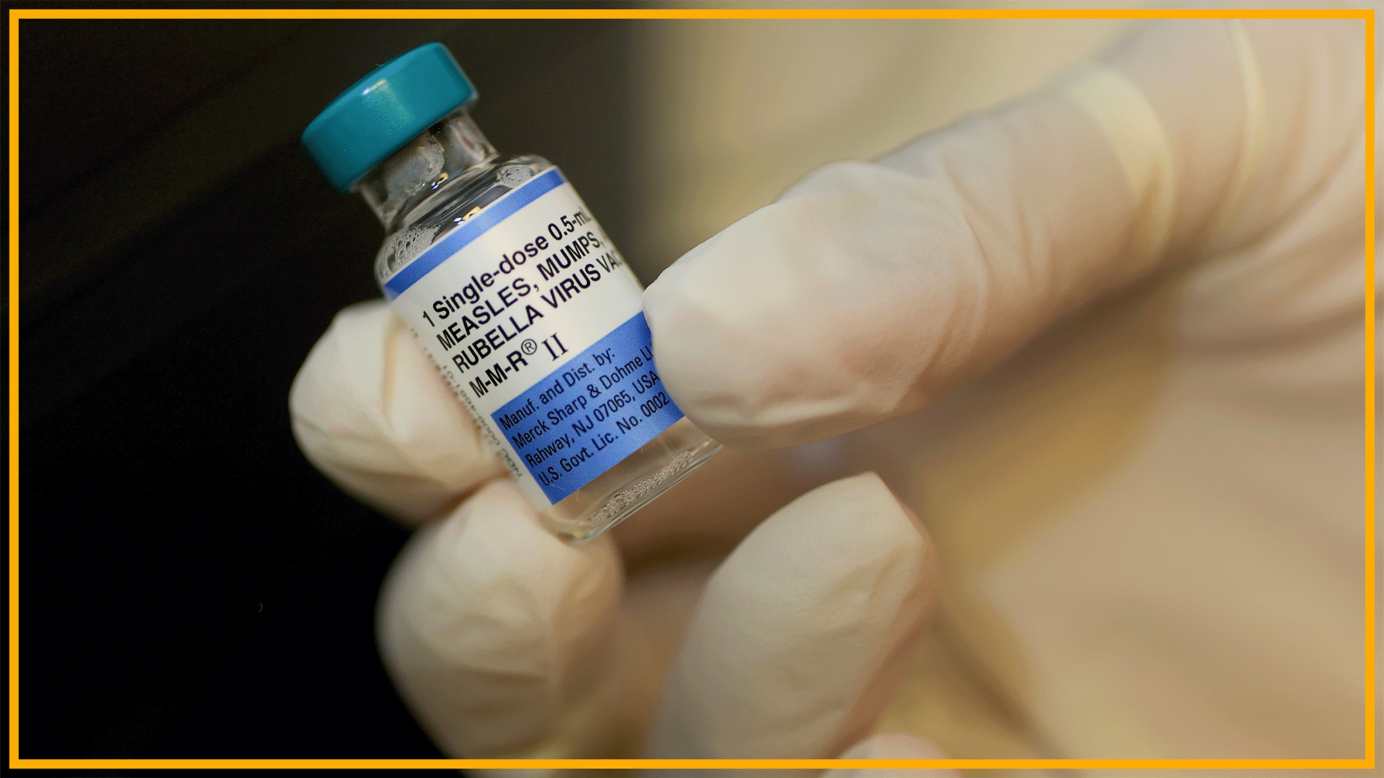 A close up of a glass bottle labeled measles vaccine being held by a gloved hand.