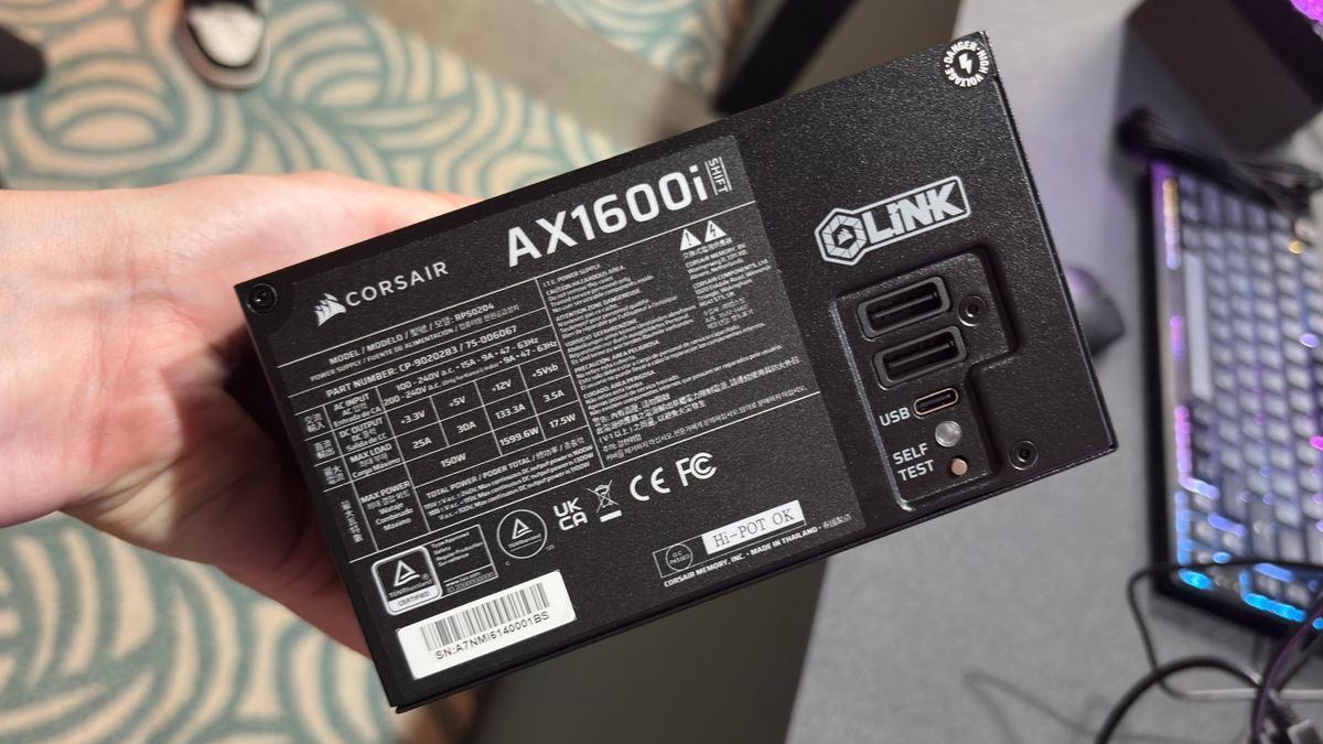 A photo of a Corsair AX1600i Shift PSU being held in a hand, showing the unit's iCUE Link and USB Type-C ports