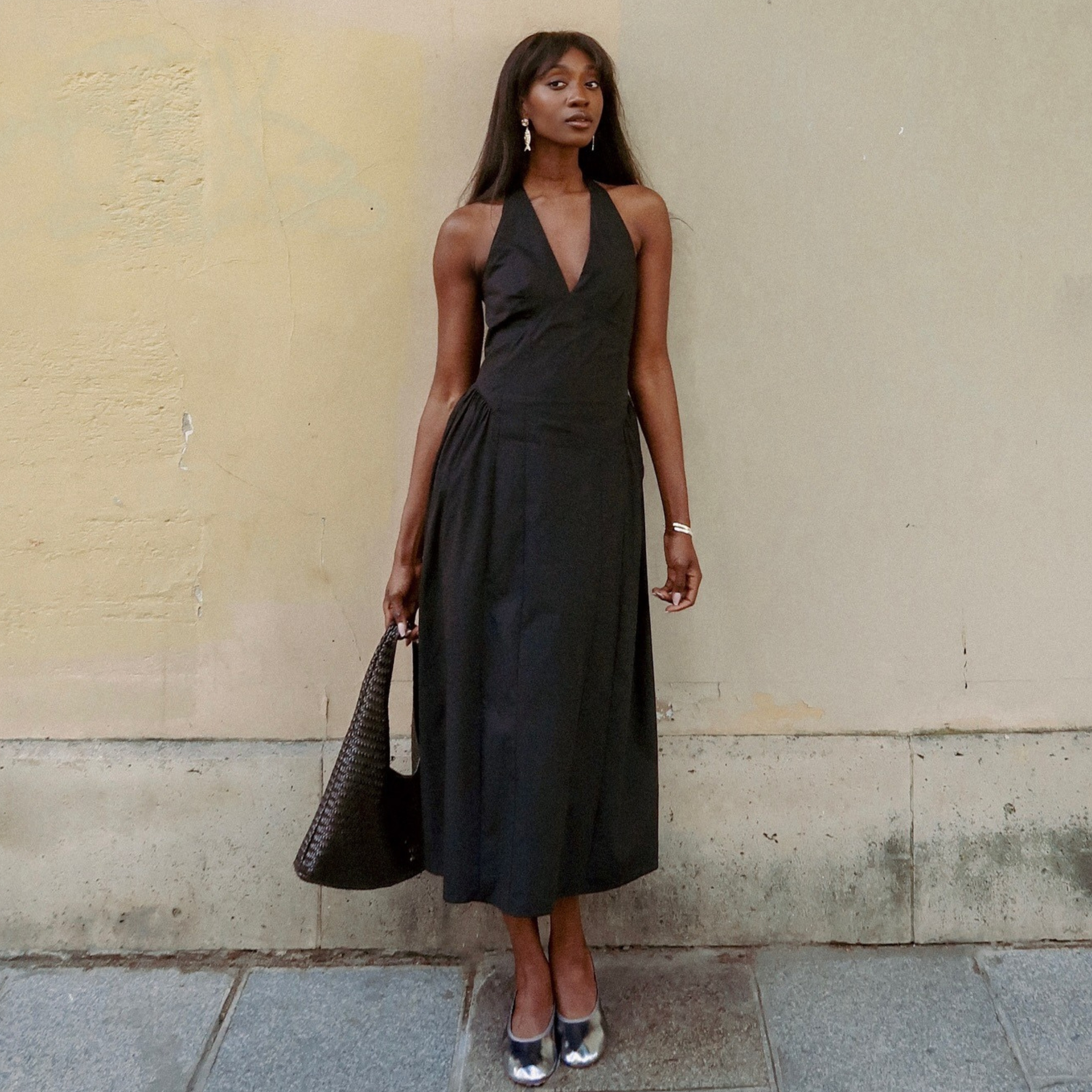 woman wears black halterneck dress stood against a wall. 