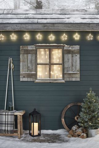 Festive green winter cabin with curtain lights, candles and festoon lights