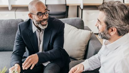 A financial adviser talks with a client on a sofa in his office.