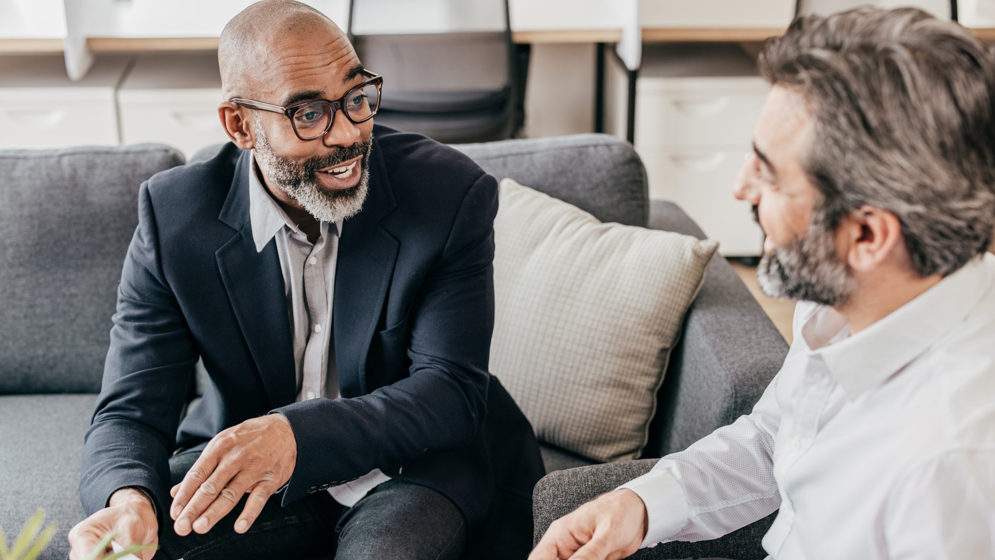 A financial adviser talks with a client on a sofa in his office.