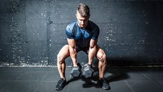 Man in squat position holding two dumbbells between legs 