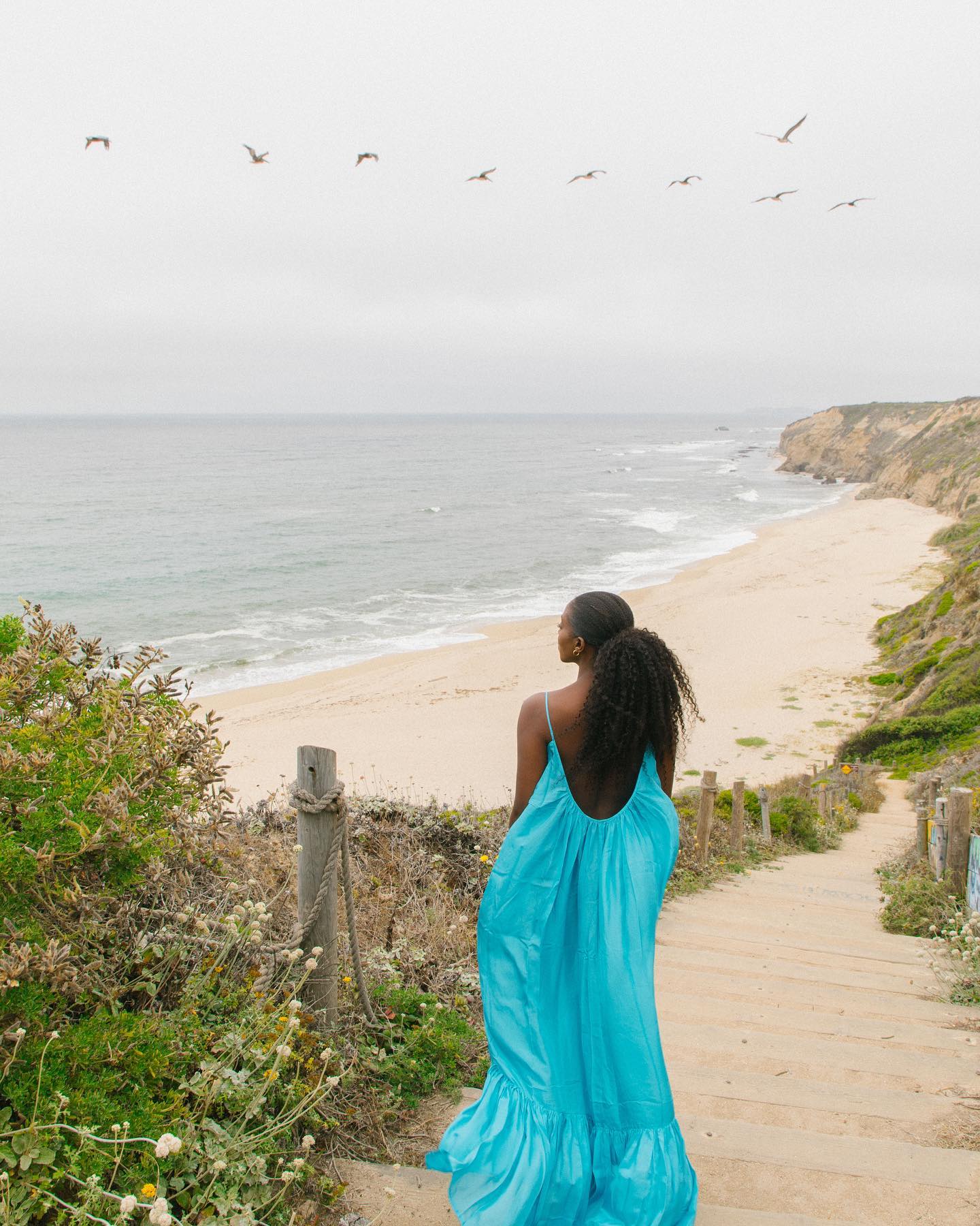 @spiritedpursuit wears an aqua blue maxi dress as she walks towards the beach