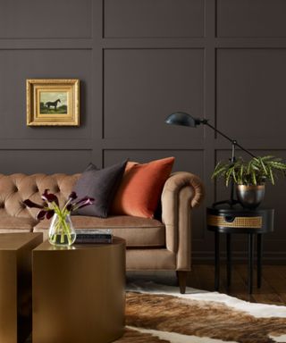 living room with dark brown walls, brown sofa and moody decor