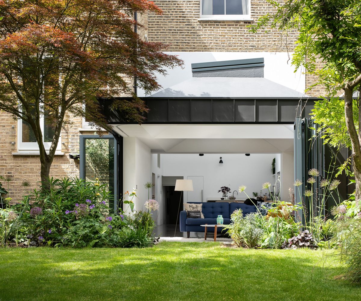 A contemporary kitchen extension with fully open bifold doors and views of a pristine garden lawn and flower beds