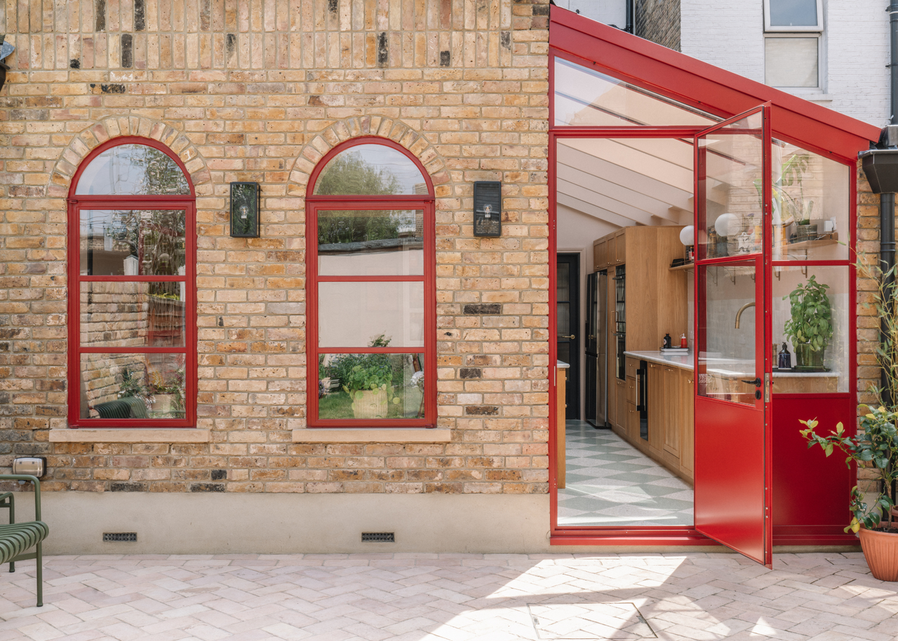 The exterior of a kitchen extension with red painted patio door and arched windows contrasting against the brick exterior wall